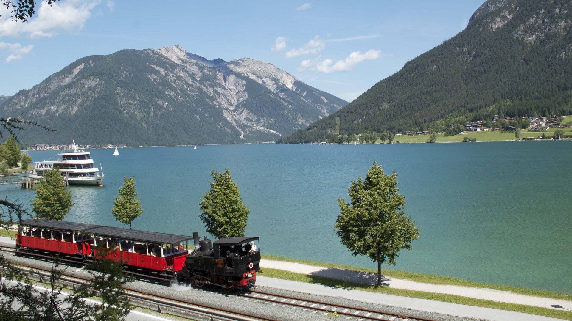 Wandern am Achensee: traumhaft schön Dampfeisenbahn fährt am Seeufer mit Bergen im Hintergrund