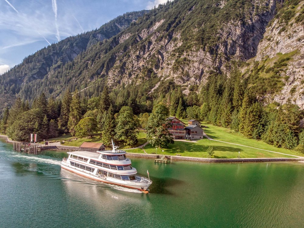 Wandern am Achensee: traumhaft schön Personenschiff fährt über grünen See vor Alpenbergen und Wäldern