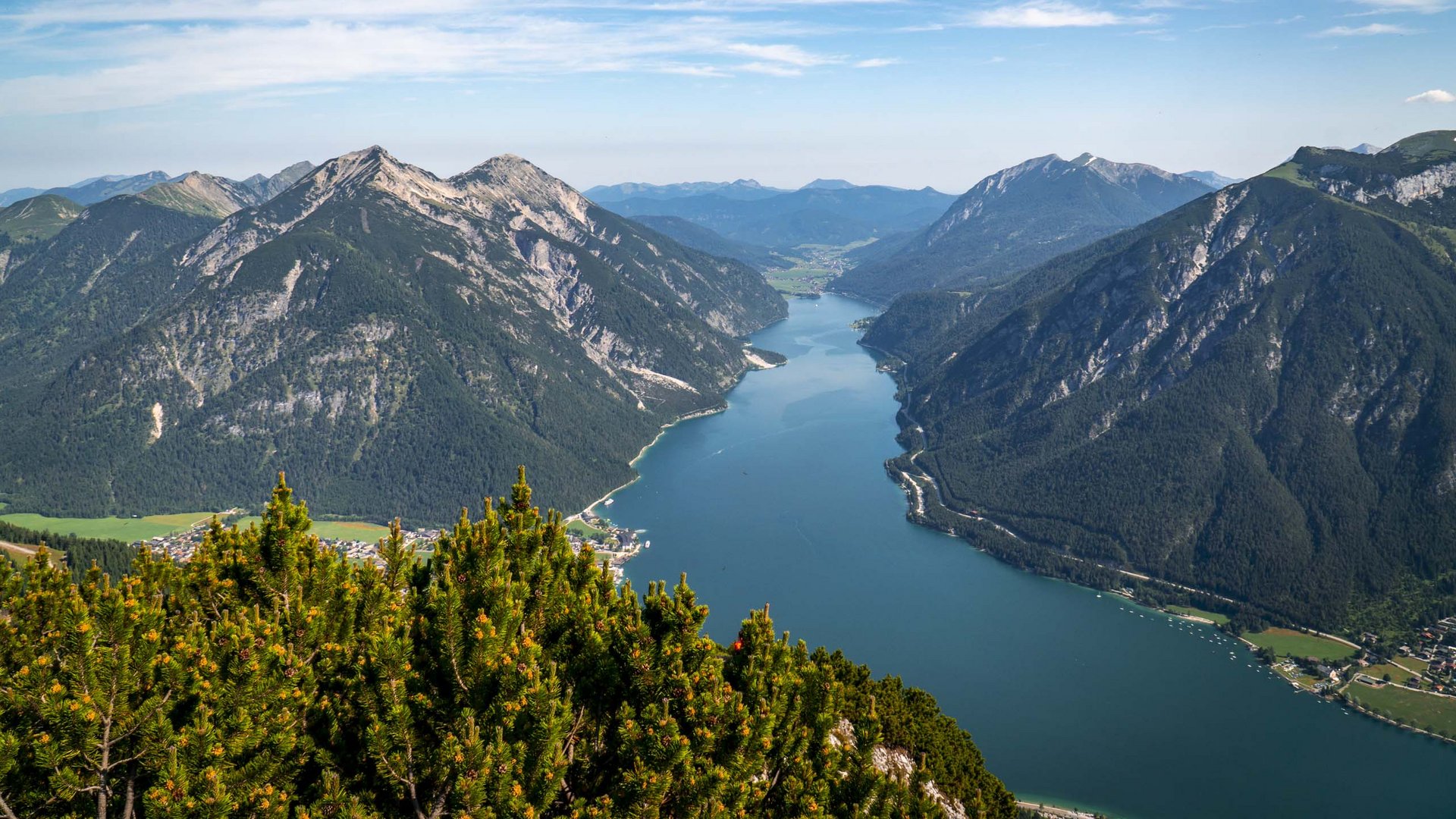 Wandern am Achensee: traumhaft schön Bergsee umgeben von bewaldeten Bergen unter blauem Himmel