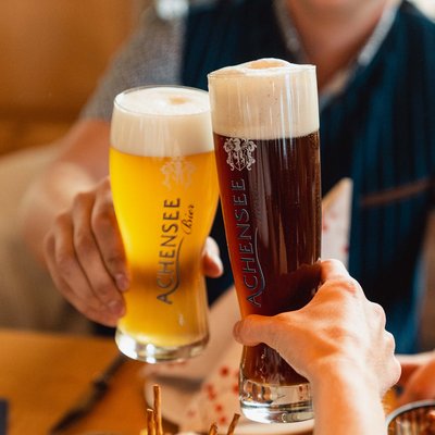 Verwöhnhotel am Achensee: Neuigkeiten Zwei Personen stoßen mit einem hellen und einem dunklen Achensee Bier an