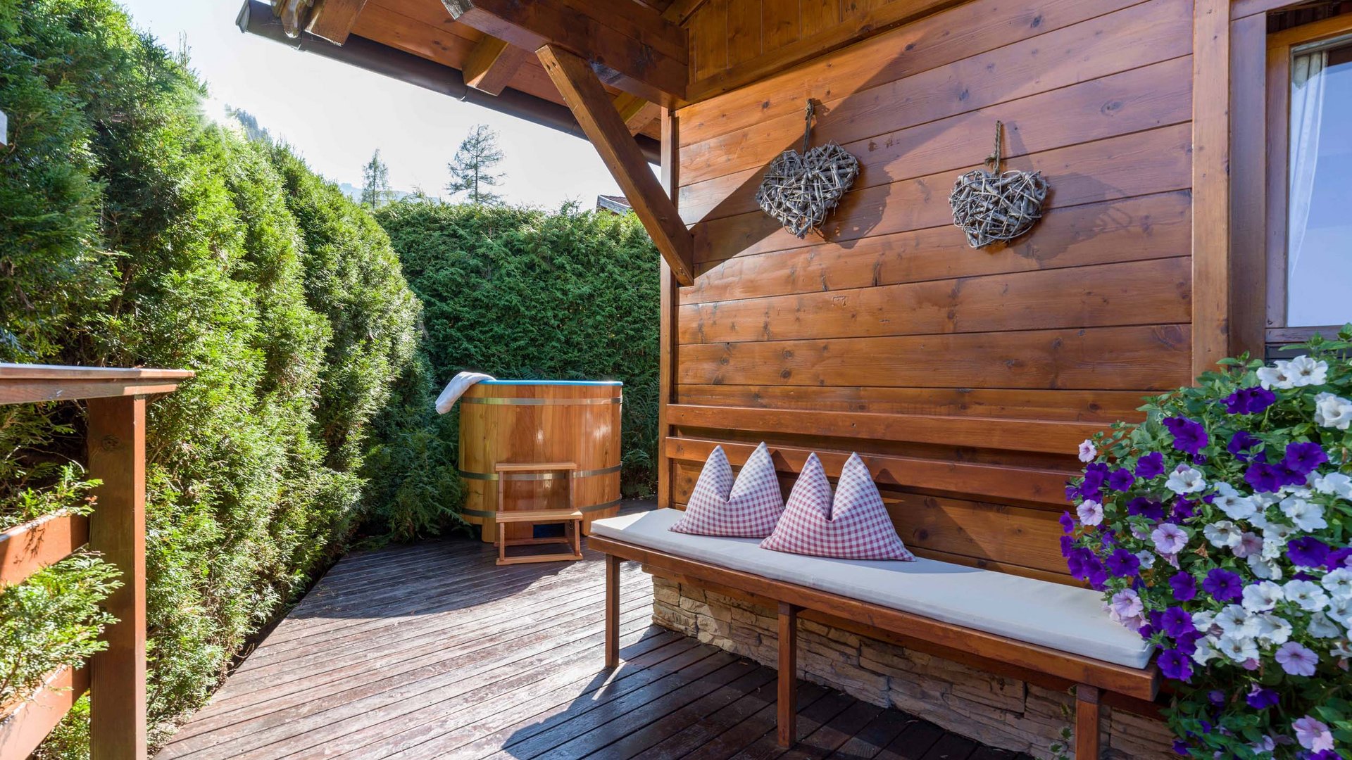 Achensee + Hotel mit Pool = Karlwirt Holzterrasse mit Bank, Holzherz-Deko und Holzwanne umgeben von Grünpflanzen