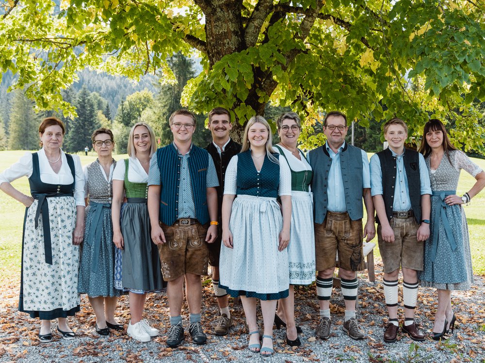 Hotel on Lake Achensee? The Karlwirt! Ten people in traditional Bavarian clothing standing under a tree in a field