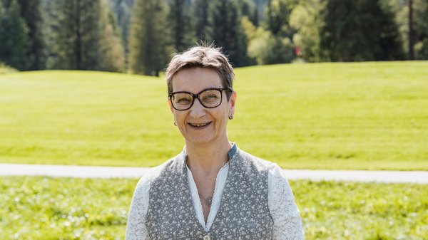 Die Karlwirt-Crew Lächelnde Frau mit Kurzhaarschnitt und Brille im Grünen vor Bäumen