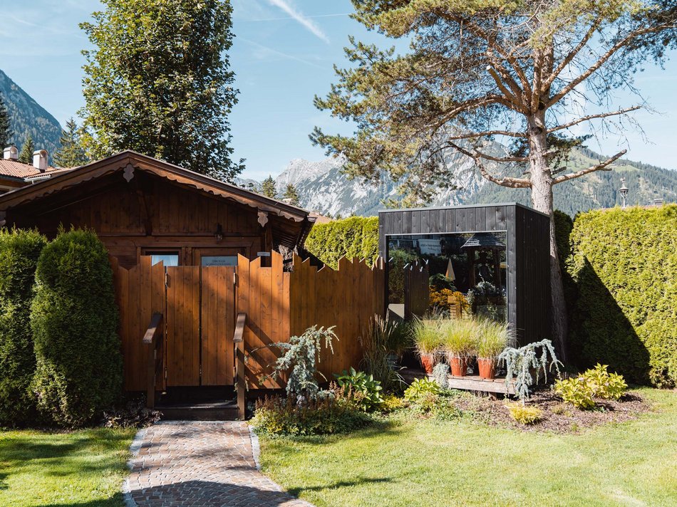 Das Hotel Karlwirt: herzlich willkommen! Garten mit Holzhütte, moderner Gartenraum und Alpen im Hintergrund bei Sonnenschein
