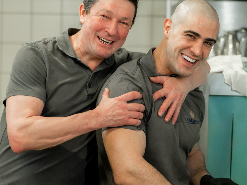 Hotel in Pertisau/Lake Achensee: join us! Two smiling men in gray polo shirts hugging each other in a kitchen