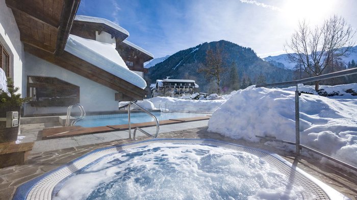 Das Hotel Karlwirt: herzlich willkommen! Outdoor-Whirlpool und Pool neben schneebedecktem Haus mit Blick auf verschneite Berge