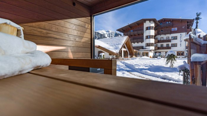 Das Hotel Karlwirt: herzlich willkommen! Blick aus Sauna auf verschneiten Hotelgarten und Berge bei Sonnenschein