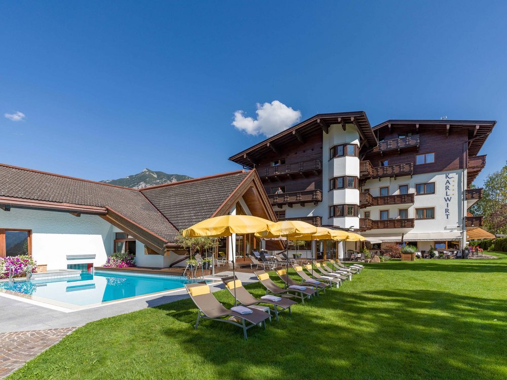 The Karlwirt in Pertisau: All this is included. Hotel with outdoor pool, lounge chairs and yellow umbrellas on a sunny day