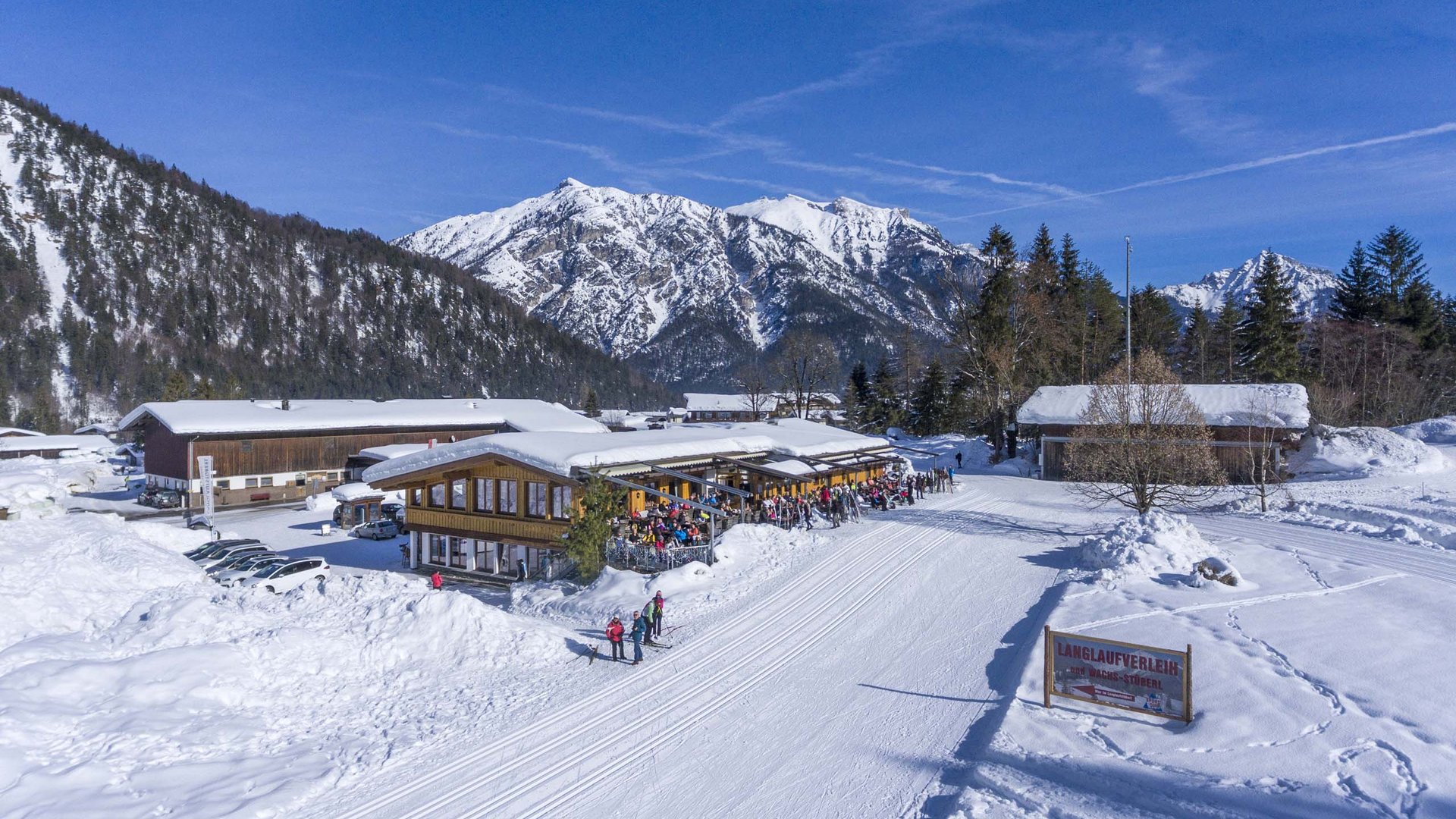Winter landscape with snow-covered mountains and ski lodge with people on sunny terrace