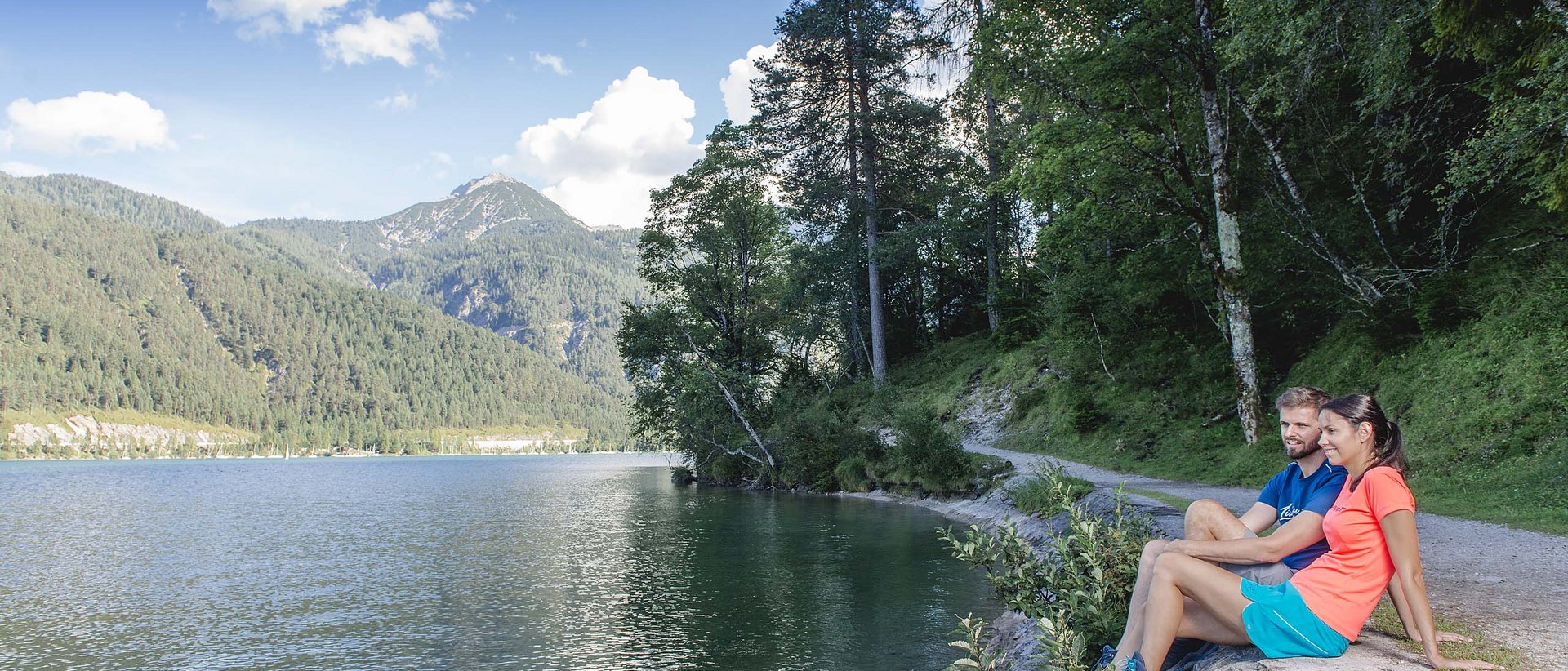 Die Achensee-Runde Paar sitzt am Seeufer mit Bergblick und Wald im Hintergrund