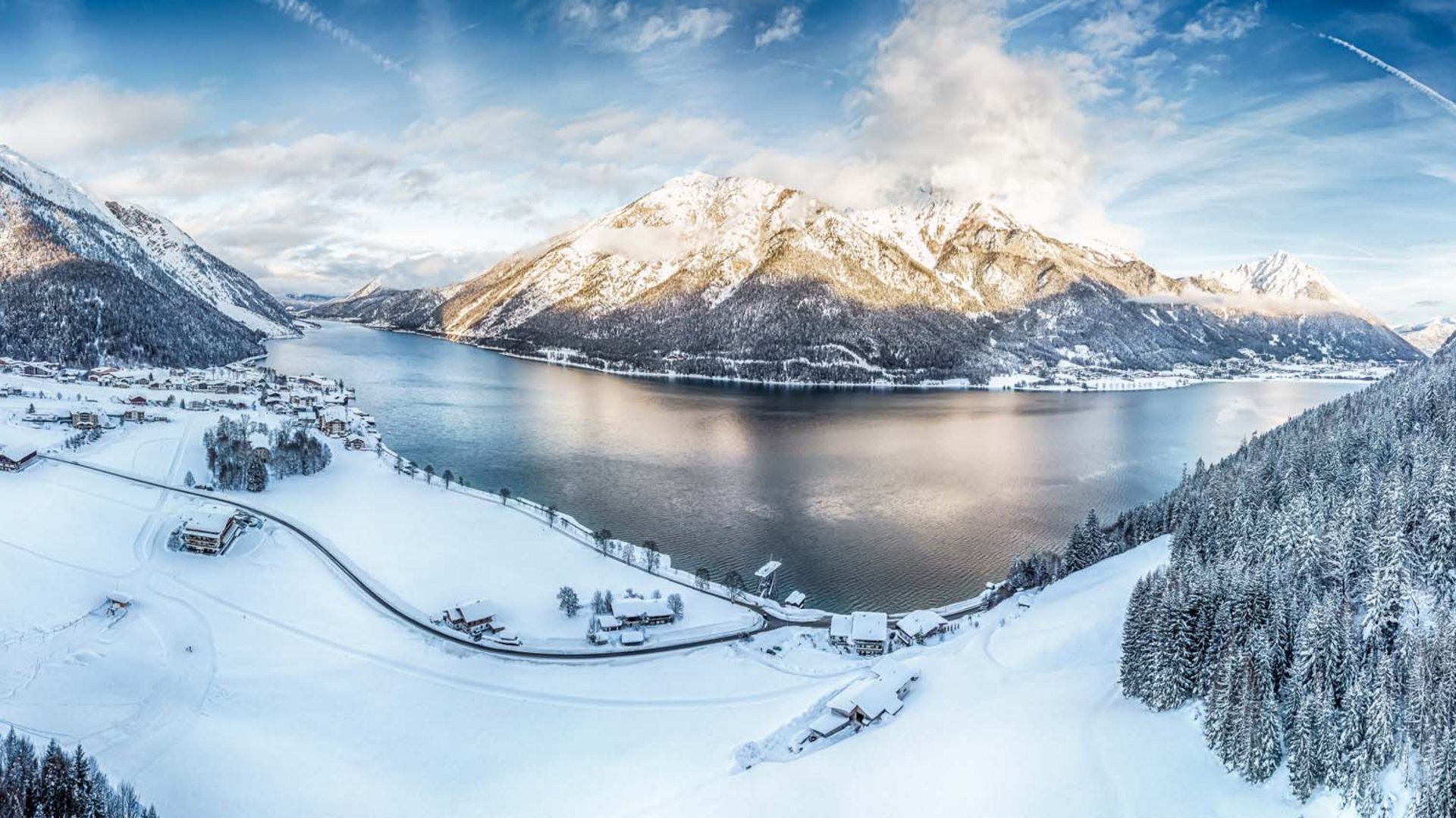 Winterlandschaft mit schneebedecktem Dorf und Bergsee unter blauem Himmel