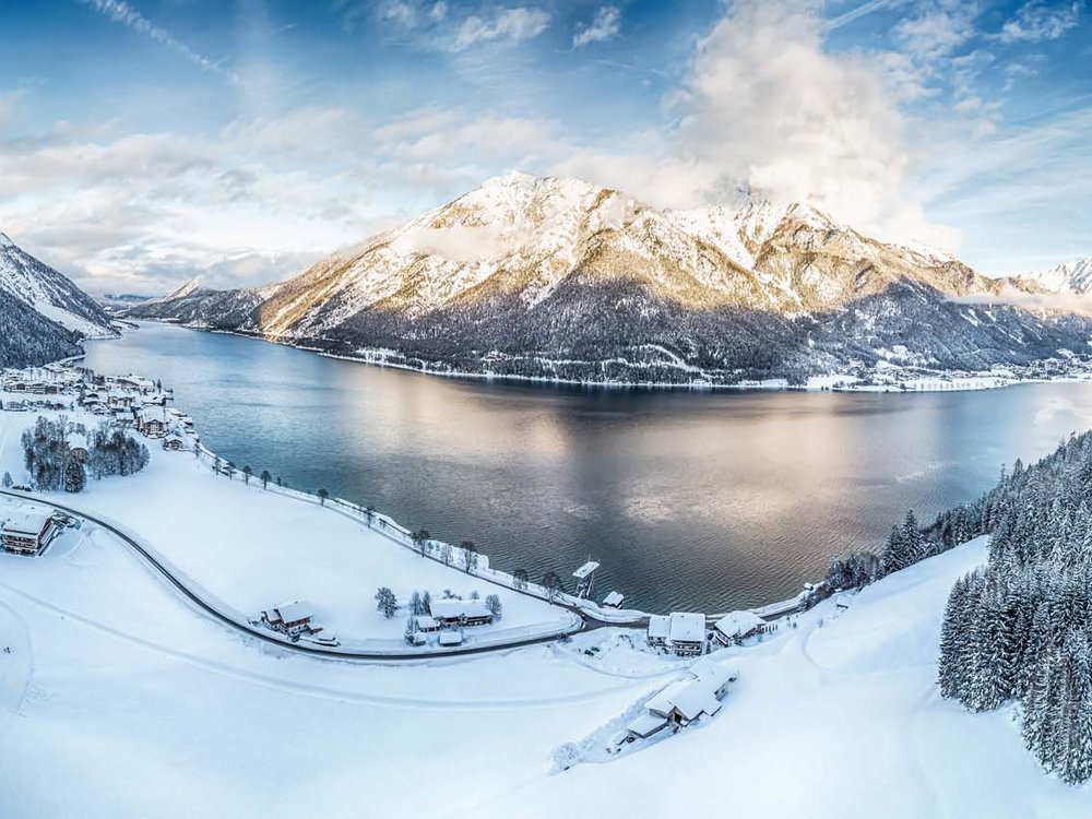 Hotel Karlwirt in Pertisau = love for the environment Winter landscape with snowy village and mountain lake under blue sky