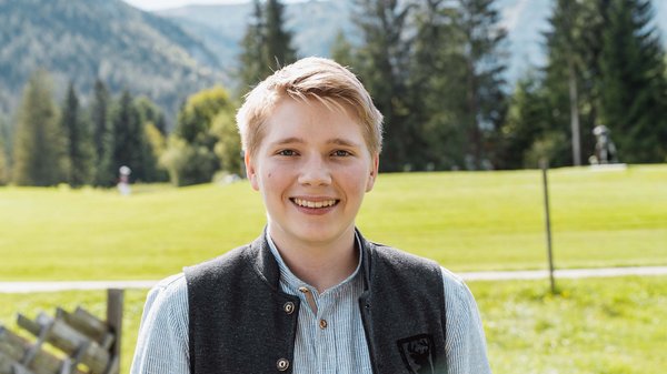 Die Karlwirt-Crew Junger Mann mit heller Weste lächelt auf einer grünen Wiese vor Bergen