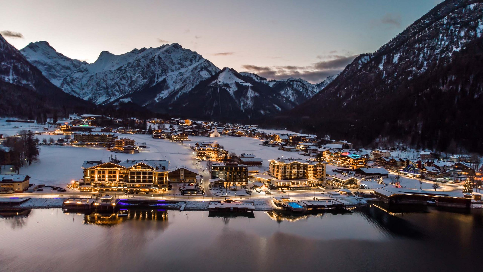 Achensee: Ausflugsziele und mehr Abendlicher Blick auf beleuchtetes Bergdorf am See mit schneebedeckten Bergen