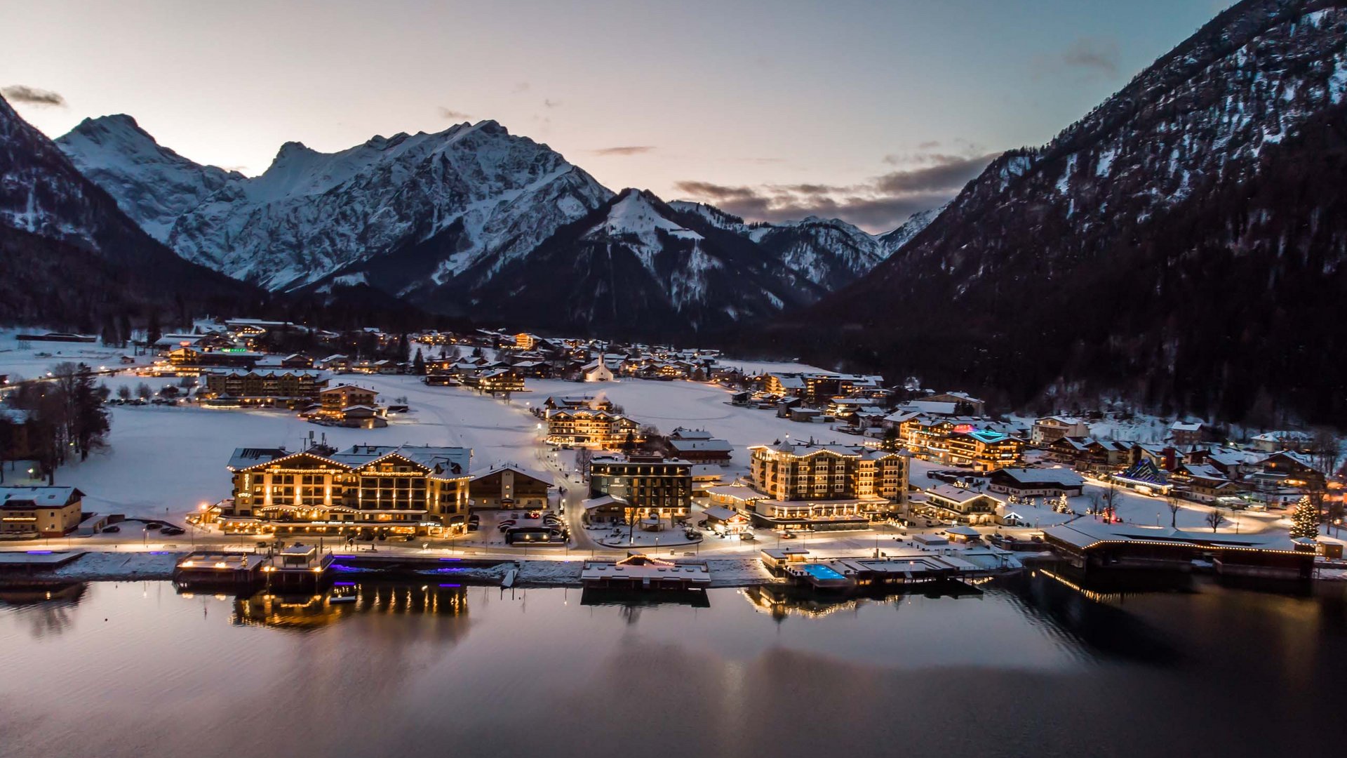 Achensee: Ausflugsziele und mehr Abendlicher Blick auf beleuchtetes Bergdorf am See mit schneebedeckten Bergen