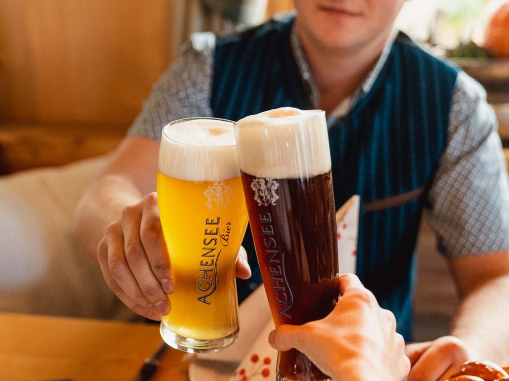 Your restaurant on Lake Achensee: the Karlwirt People clinking glasses of light and dark Achensee beer with traditional snacks including pretzels