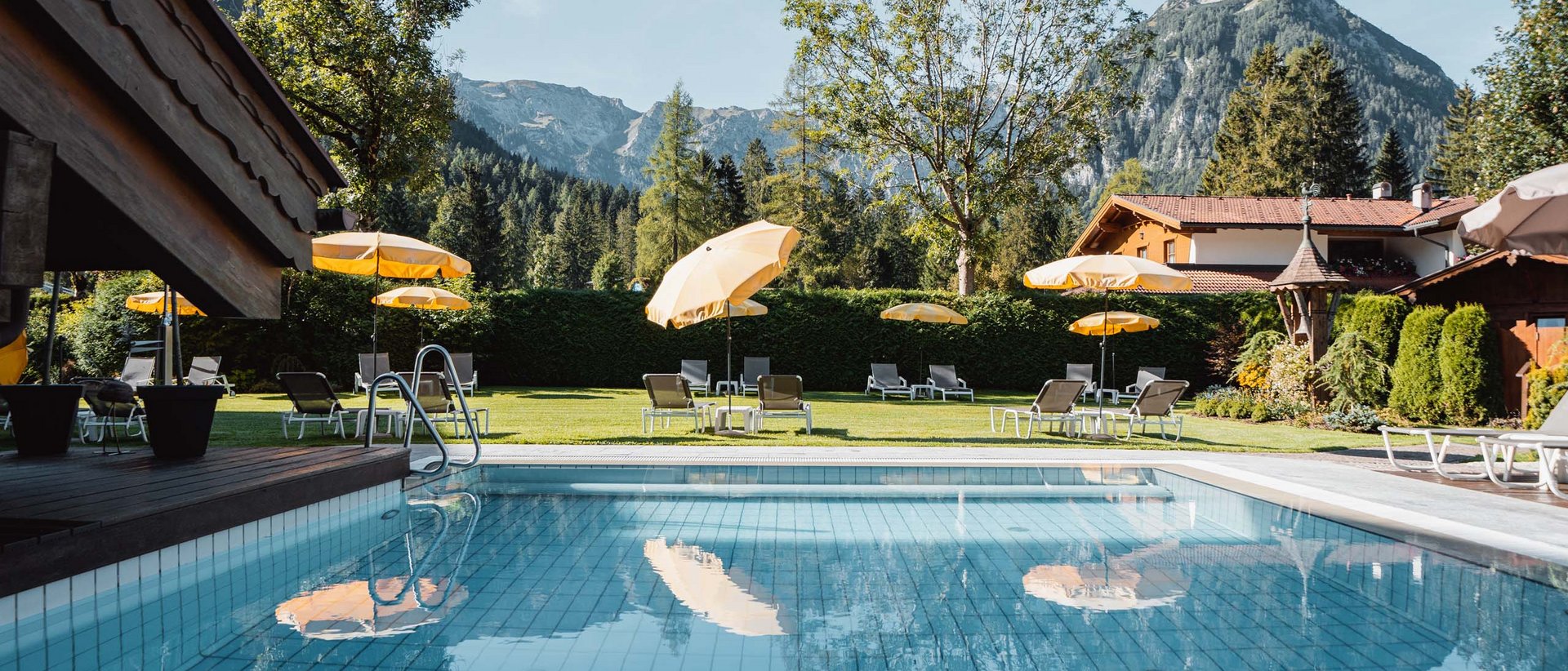Das Schwimmen und seine positive Wirkung Pool mit gelben Sonnenschirmen vor Berglandschaft und Haus