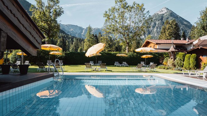 Das Hotel Karlwirt: herzlich willkommen! Pool mit gelben Sonnenschirmen vor Berglandschaft und Haus