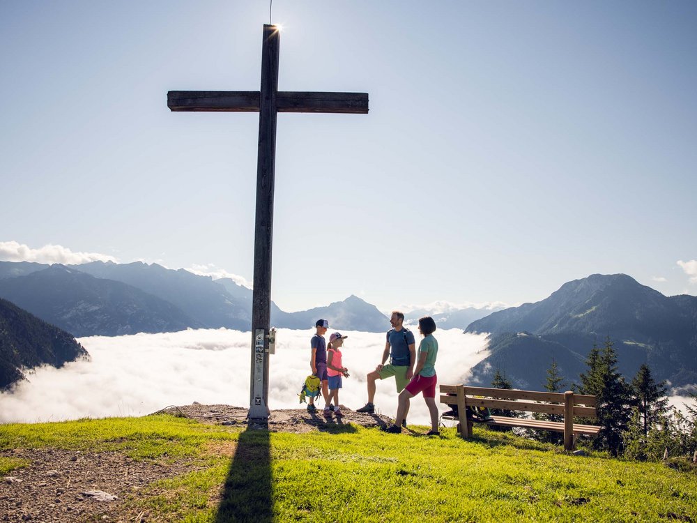 Achensee: Ausflugsziele und mehr Familie steht bei großer Holzkreuz mit Berg- und Wolkenlandschaft im Hintergrund