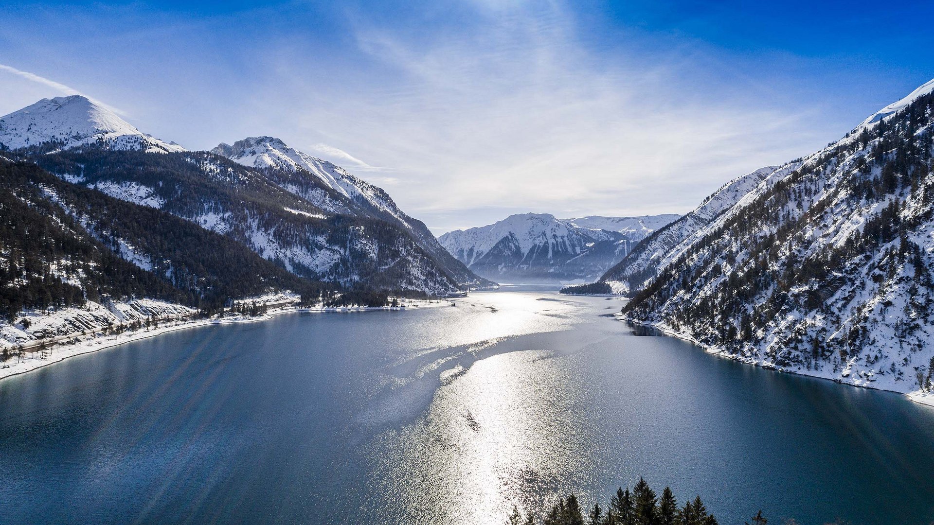 Our hotel on Lake Achensee with swimming pool Mountain lake with snow-covered peaks and bright sunlight