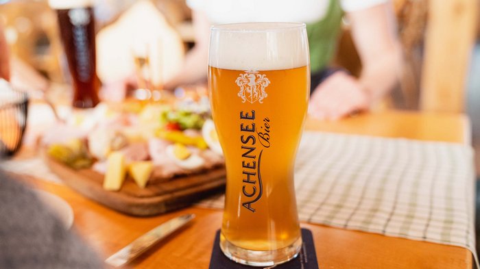 Das Achenseebier des Karlwirt Ein Glas Achensee Bier auf einem Tisch mit einer Brotzeit im Hintergrund
