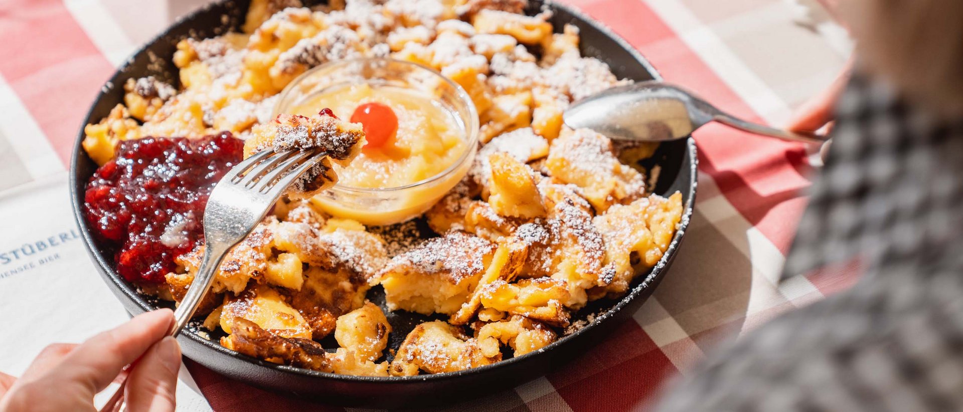 Kulinarische Vielfalt Person isst Kaiserschmarrn mit Apfelmus und Preiselbeeren aus Pfanne
