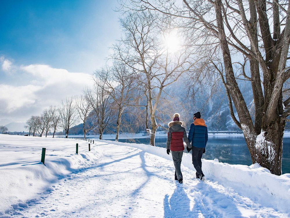 Skifahren am Achensee und mehr Paar hält Händchen und spaziert im verschneiten Winter am See entlang