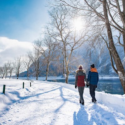Das Hotel Karlwirt: herzlich willkommen! Paar hält Händchen und spaziert im verschneiten Winter am See entlang