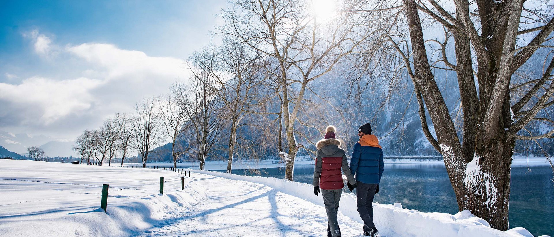 Feiert das Fest der Liebe im Hotel Karlwirt. Paar hält Händchen und spaziert im verschneiten Winter am See entlang