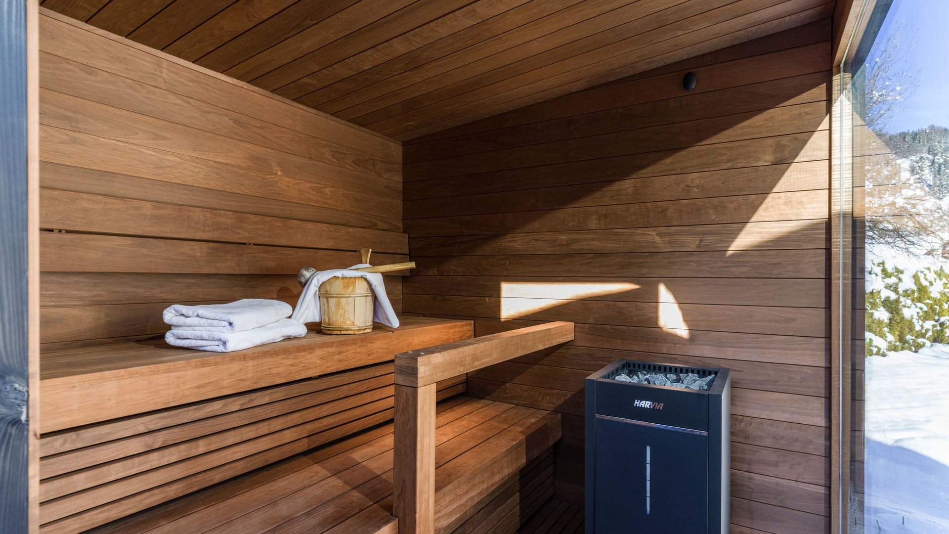 Wellnesshotel am Achensee: Karlwirt Moderne Sauna mit Holzbanken, Handtüchern und Blick auf schneebedeckte Landschaft