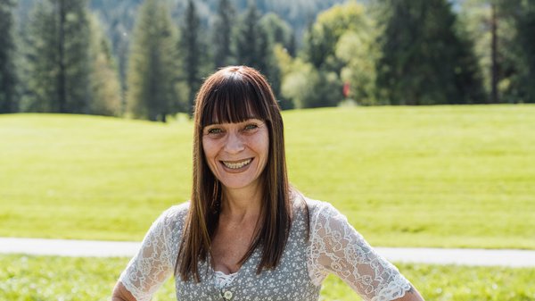 Die Karlwirt-Crew Frau mit braunen Haaren in Trachtenkleidung lächelt vor grüner Wiese und Wald