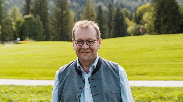 Die Karlwirt-Crew Lächelnder Mann in Brille und Weste vor grüner Wiese und Wald