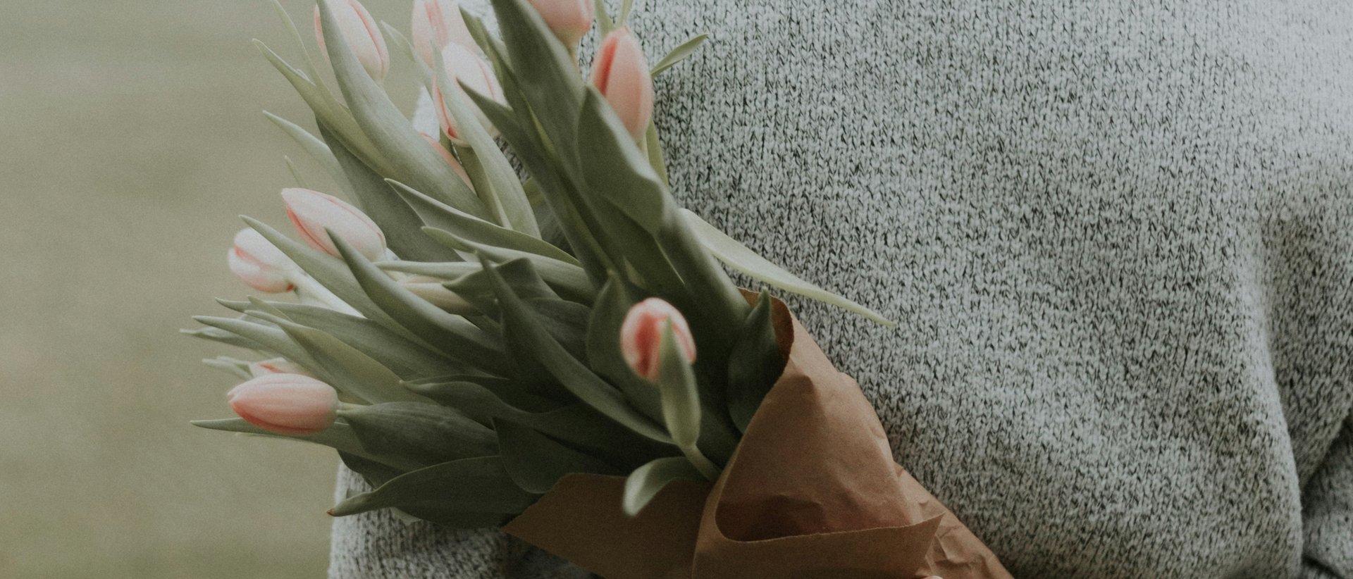 Warum ein Gutschein vom Karlwirt mehr sagt als Blumen Frau mit roten Haaren hält blühenden Tulpenstrauß hinter Rücken im Freien