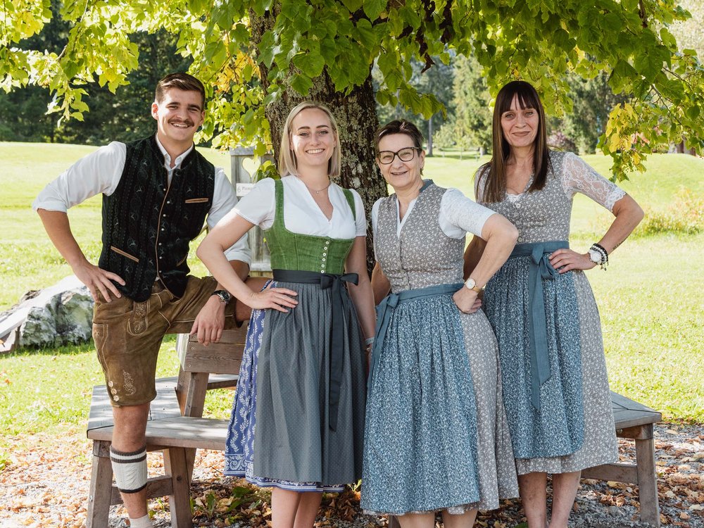 Die Karlwirt-Crew Vier Personen in traditioneller bayerischer Tracht stehen vor einem Baum im Freien