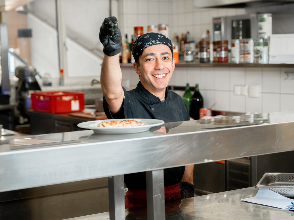 Hotel in Pertisau/Lake Achensee: join us! Smiling chef in kitchen serving a plate of pasta