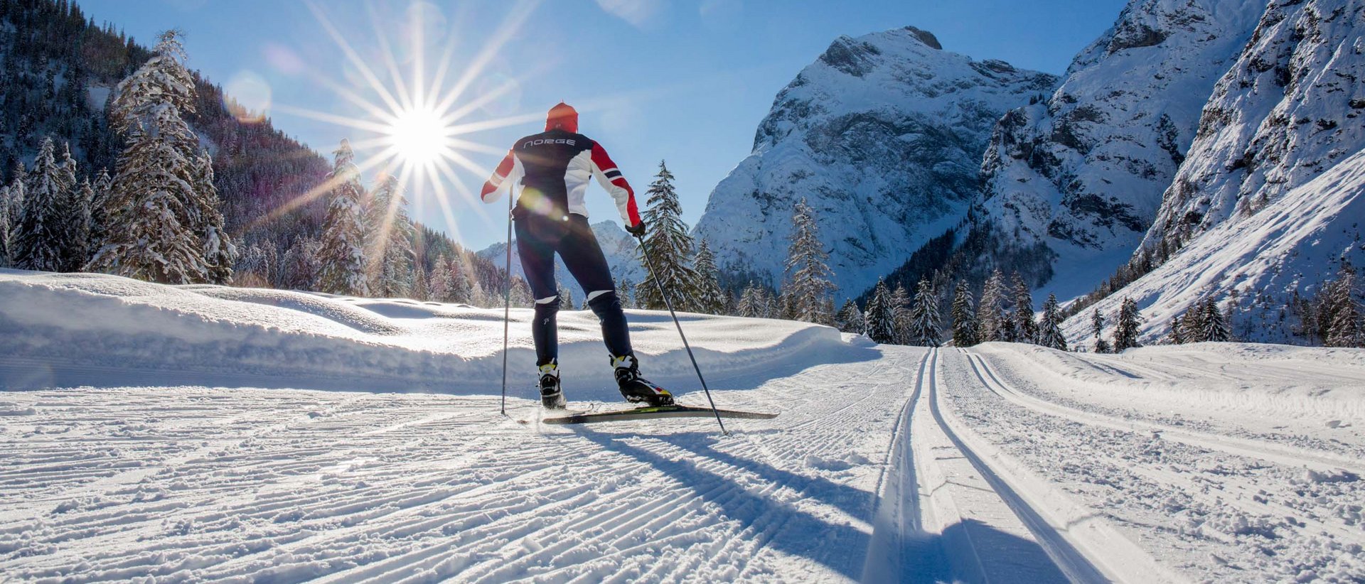 Wintersport am „Tiroler Meer“ Langläufer im Winter auf verschneiter Spur mit Bergen und Sonne im Hintergrund