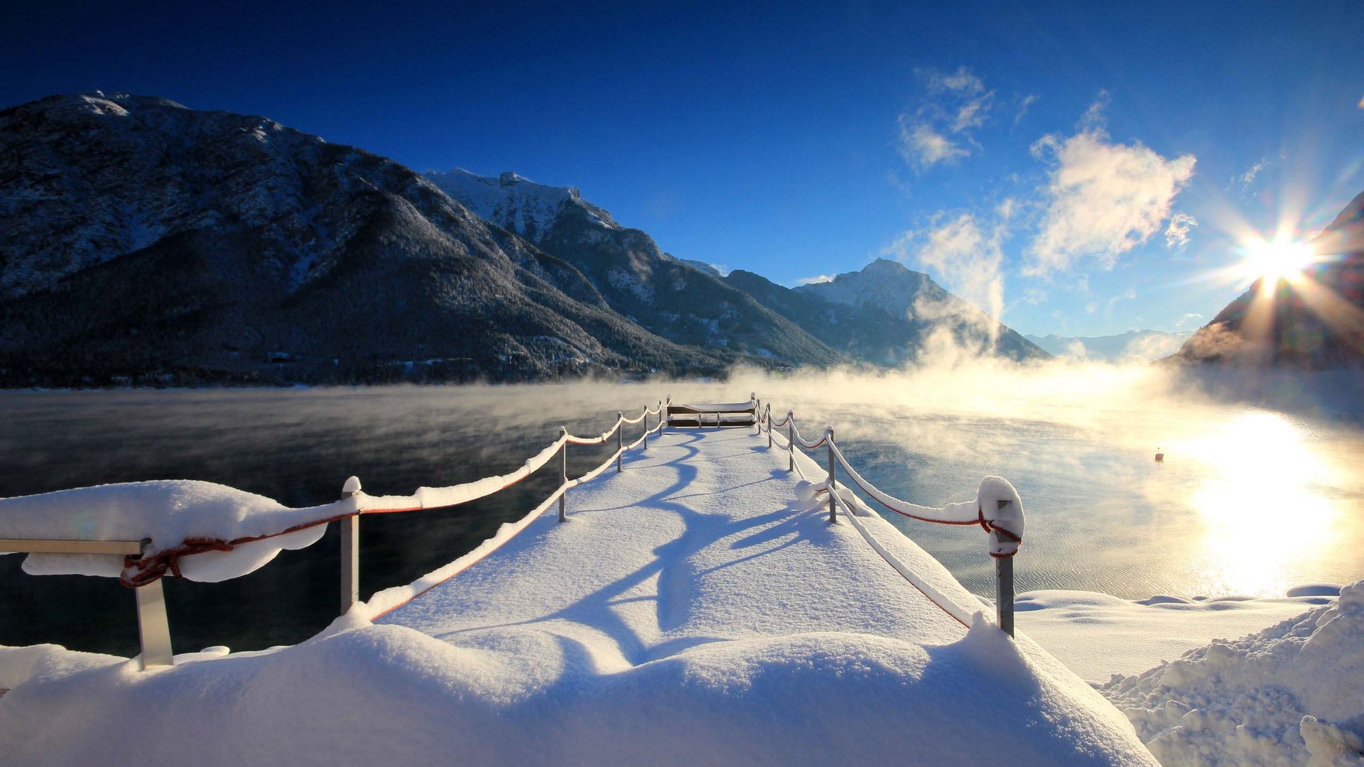 Achensee: Ausflugsziele und mehr Schneebedeckter Steg an einem winterlichen, nebligen Bergsee bei Sonnenaufgang