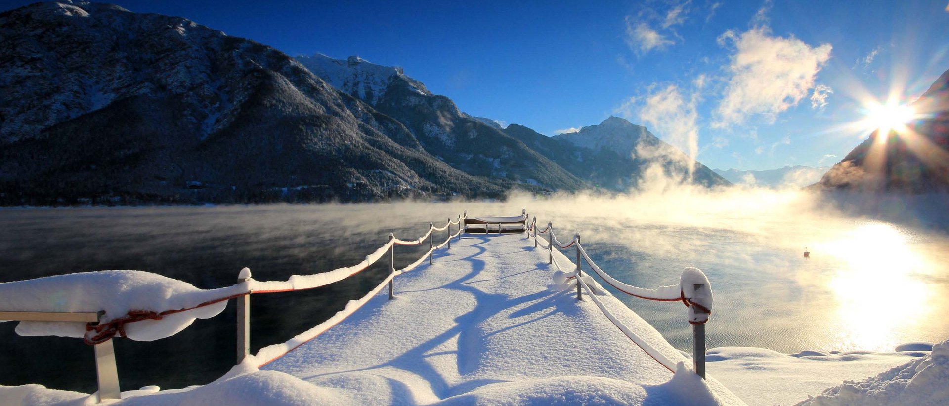Urlaub im Winterwunderland Schneebedeckter Steg an einem winterlichen, nebligen Bergsee bei Sonnenaufgang