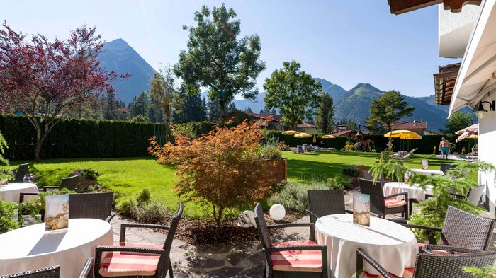 Das Hotel Karlwirt: herzlich willkommen! Sonnige Terrasse mit Tischen, Stühlen und Bergblick im Garten