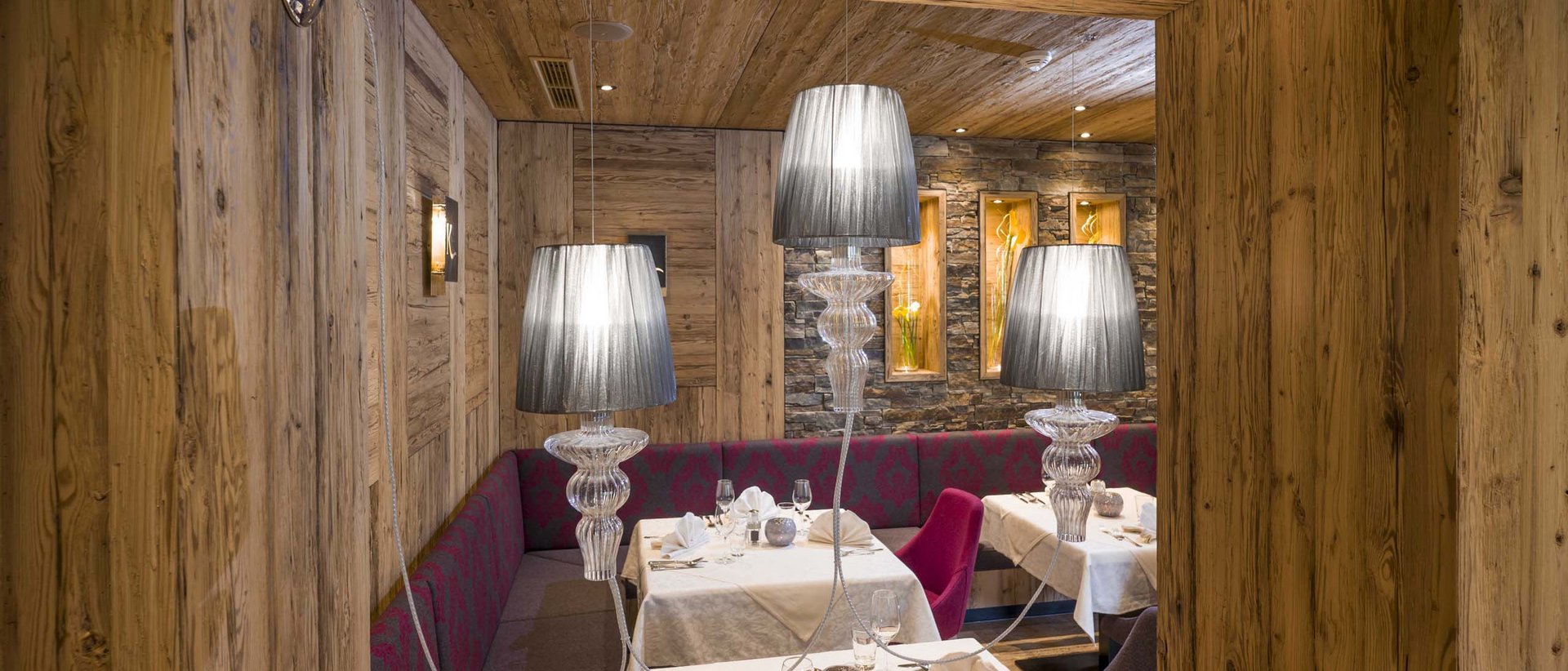 Tiroler Kräuternocken Gemütlicher Restaurantbereich mit Holzwänden und gedeckten Tischen mit Lampen