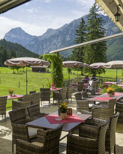 Das Restaurant am Achensee: Karlwirt Terrasse mit Tischen und Stühlen vor Berglandschaft mit Wiesen und Bäumen