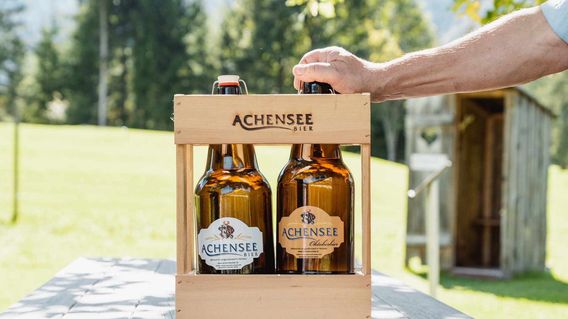 Das Achenseebier des Karlwirt Zwei Flaschen Achensee Bier in einem Holzträger auf einem Holztisch im Freien