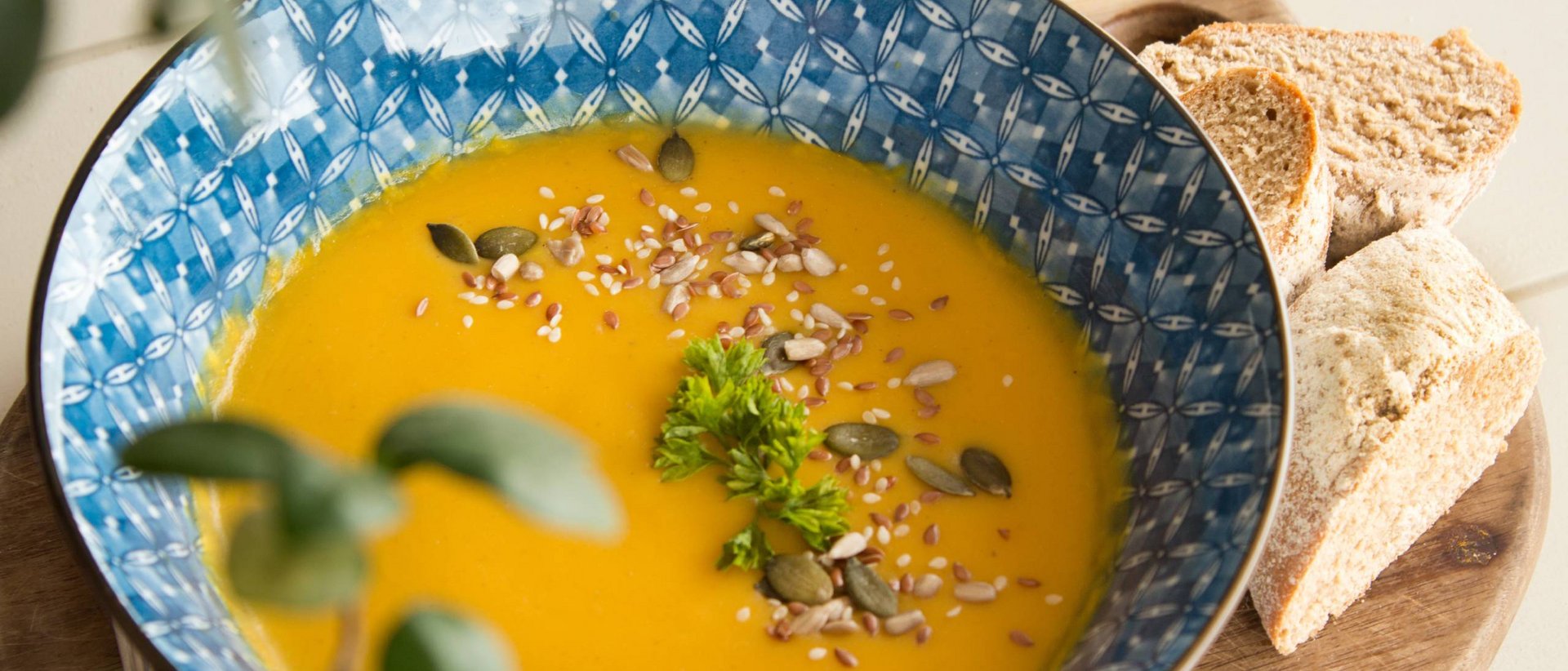 Unser Herbstrezept Kürbissuppe mit Samen und Brot auf einem Holzbrett
