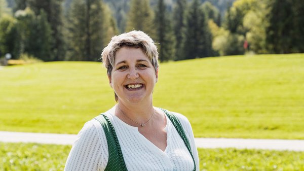 Die Karlwirt-Crew Lächelnde Frau in traditioneller Tracht vor grünem Feld und Wald