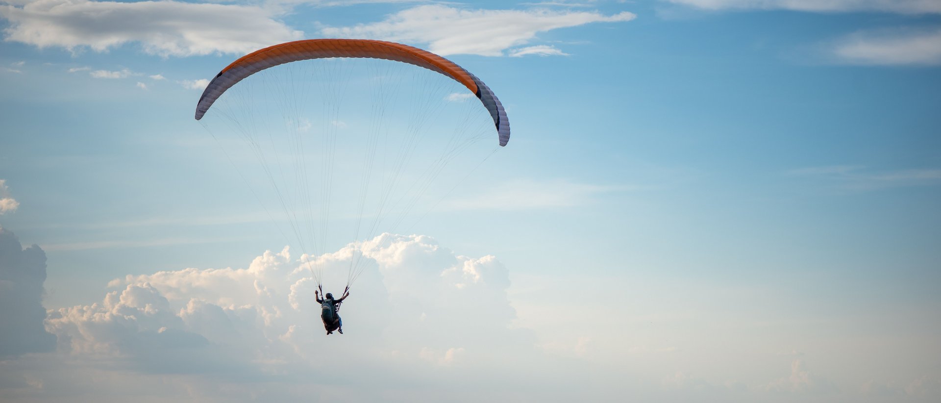 Der Adrenalinkick mit Aussicht Gleitschirmflieger vor blauem Himmel über einer Berglandschaft
