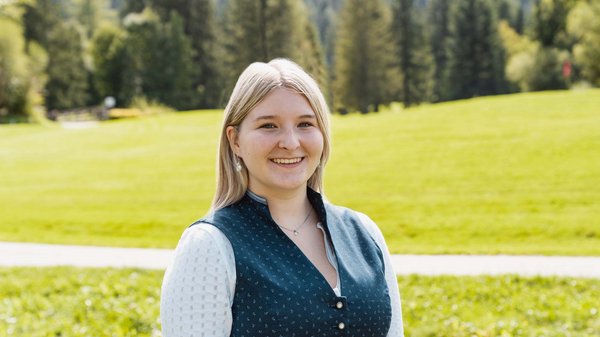 Die Karlwirt-Crew Junge Frau in traditioneller Tracht vor grünem Wiesen- und Waldhintergrund