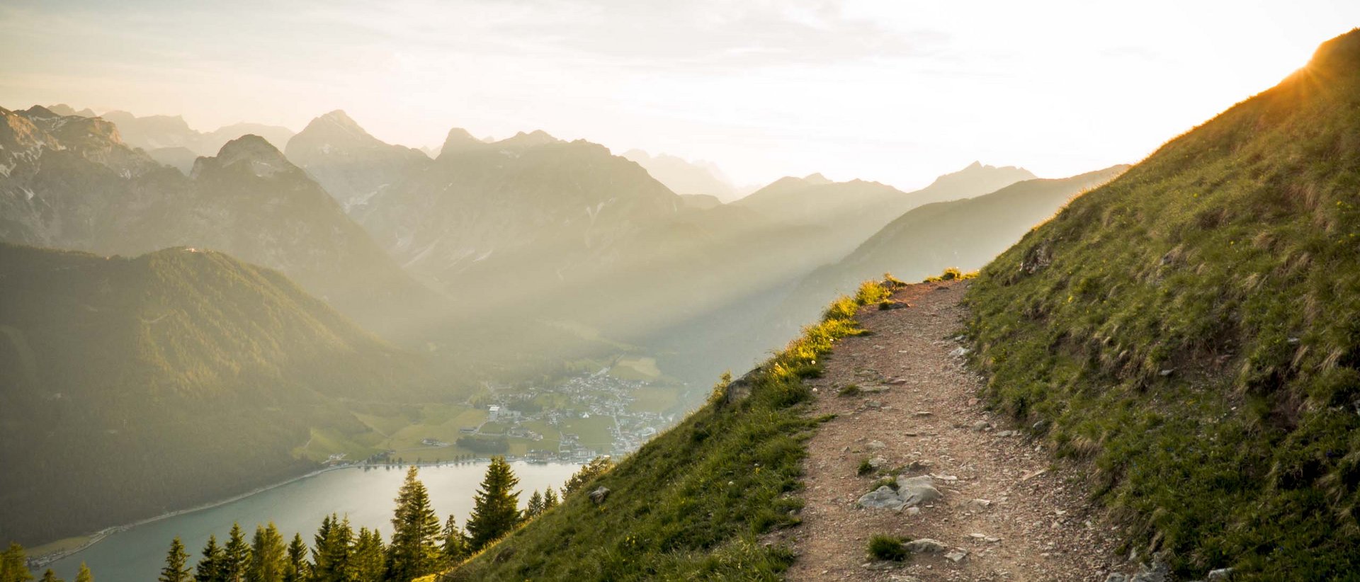 Faszinierende Ausflugsziele für den Herbst Wanderweg auf Berghang mit Blick auf Tal, See und Berge bei Sonnenuntergang
