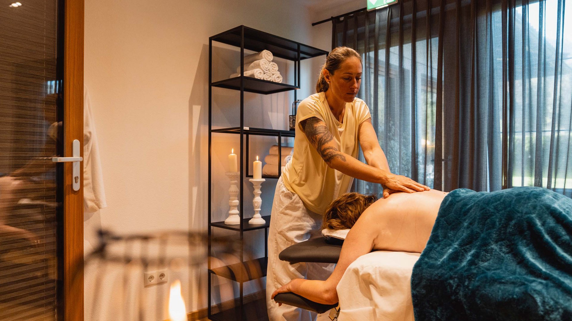 Wellnesshotel am Achensee: Karlwirt Frau erhält Rückenmassage in einem gemütlichen Wellnessraum mit Kerzenlicht