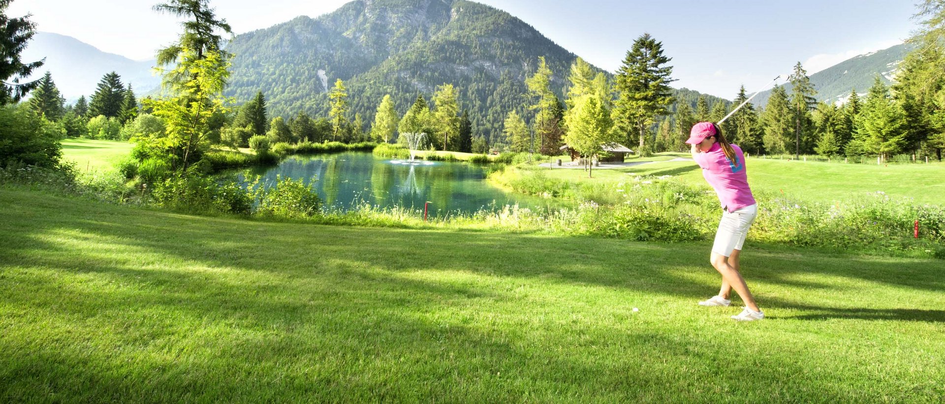 Golfen am Achensee Frau spielt Golf auf grünem Platz mit Berg und Teich im Hintergrund