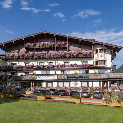 Hotel Karlwirt: a warm welcome! Hotel building with flowers and cars parked in front in the Alps